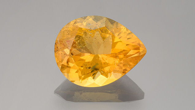 Figure 1. This 4.63 ct chondrodite contained irregular multiphase and reflective iridescent platelets with a bright orangy yellow color. Photo by Adriana Gudino; courtesy of Bill Vance.