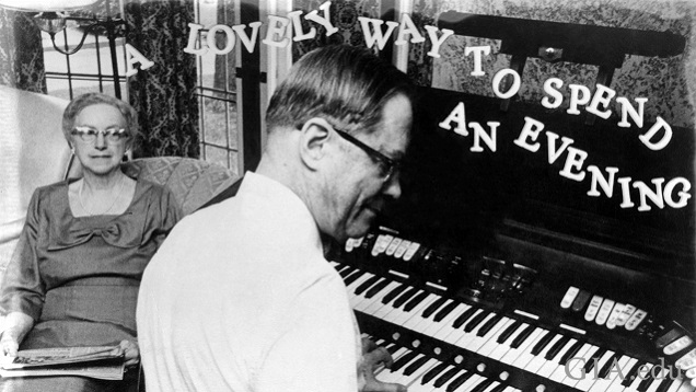 A woman sits and listens as a man plays an organ.