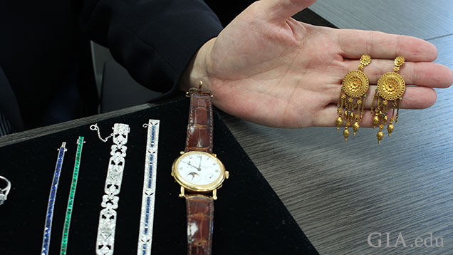 A tray of jewelry pieces sits on the desk and a hand holds a pair of Castellani earrings.