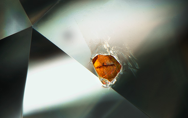 An orange rutile crystal breaks the surface of a diamond.