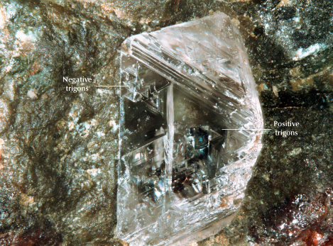 Figure 2. Partially exposed diamond embedded in an eclogite xenolith, with positive and negative trigons on the octahedral face. A mineral is included within the diamond, visible through the octahedral face. Photomicrograph by Matthew Hardman; field of view 5.74 mm.