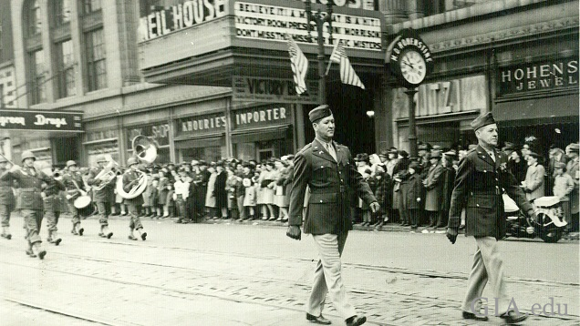 Soldiers and a band marches on a retail street.