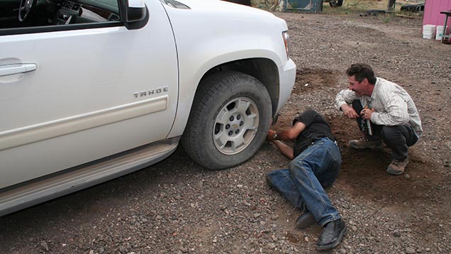 Kevin Schumacher watches as Dust Devil’s Terry Clark labors to fix a flat front tire on the team’s SUV. 