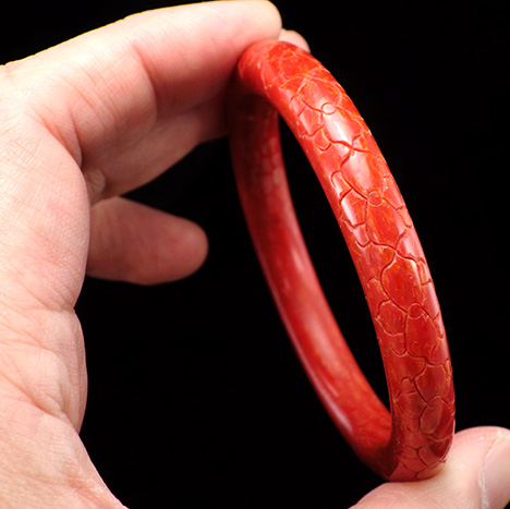 Carved bangle composed of a coral-epoxy composite.