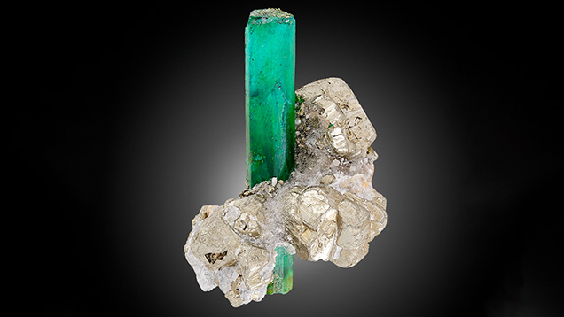 Figure 3. An assemblage of plastic and various minerals imitating rough emerald in matrix, measuring approximately 51.79 mm in height. Photo by Michele Wong.