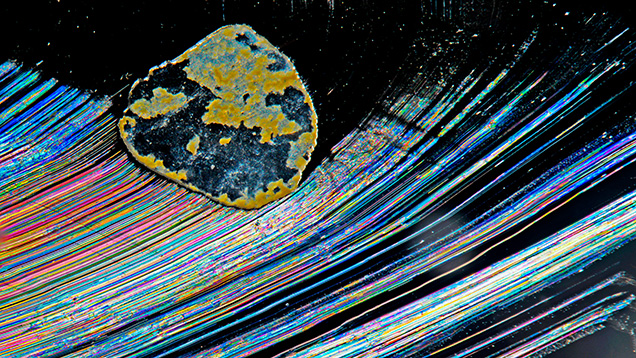 This scene of an iron stain and numerous curved lines showing rainbow colors in a fracture resembles a scene from the night sky viewed through a telescope rather than a microscope. Photomicrograph by Charuwan Khowpong; field of view 2.85 mm.