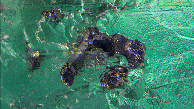 Figure 2. A combination of optical microscopy and Raman analysis identified the opaque silvery gray monoclinic inclusions as the very rare sulfide geocronite. Photomicrograph by Nathan Renfro; field of view 2.39 mm.