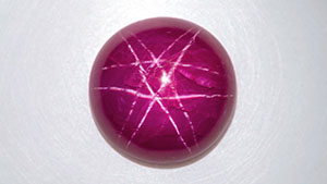 Figure 1. This unheated 11.43 ct purplish red round ruby cabochon displayed a white twelve-rayed double-star phenomenon. Photo by Nuttapol Kitdee.