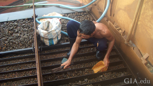 Mine worker crouches over trays of findings to clean and sort them.