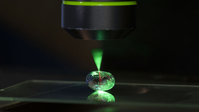 Figure 1. Microscope-assisted photoluminescence spectroscopy is an important technique for collecting data in gemological research and identification. Here, a 514 nm laser illuminates a sapphire sample at room temperature, creating red luminescence caused by trace amounts of chromium. Photo by Kevin Schumacher.